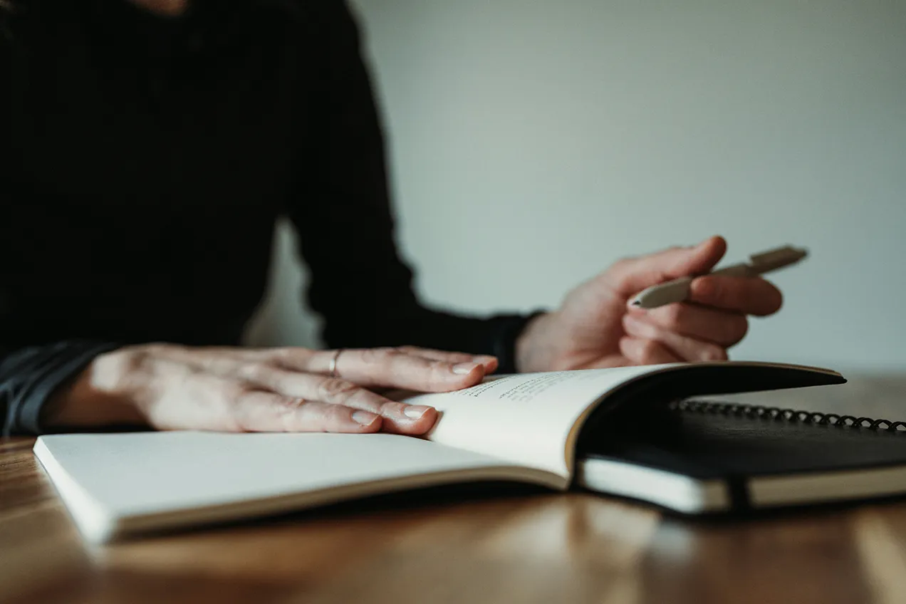 book spread open on wooden desk with hand holding a pen